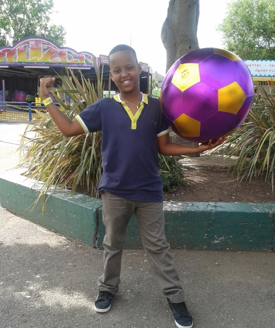 Young Eddie at a funfair, proudly holding a large purple and gold football with his fist raised