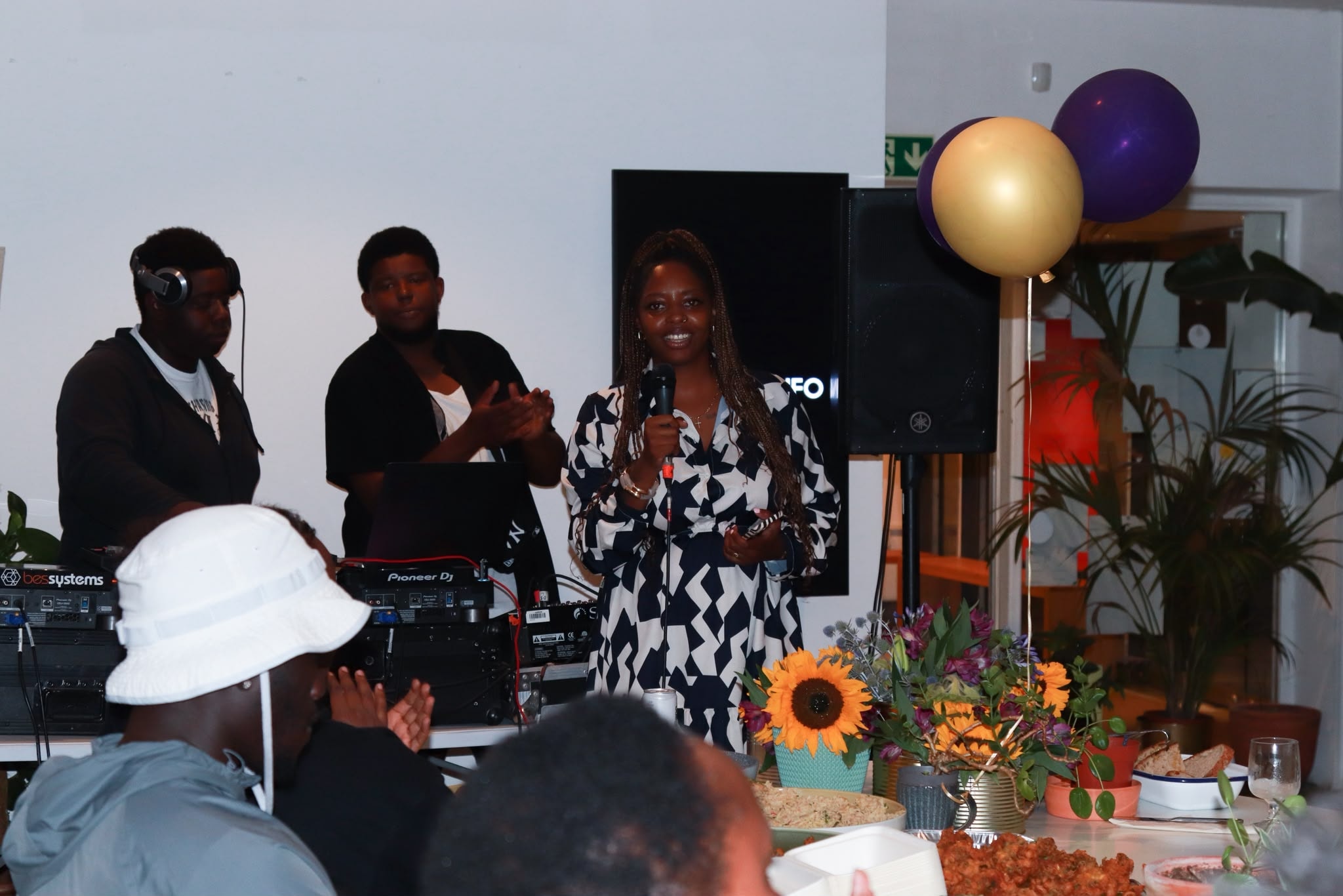 A woman addresses the room at the EKing Foundation event, purple and gold balloons behind her