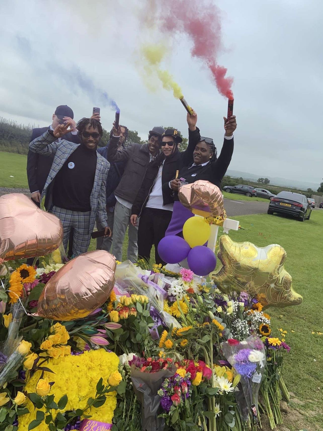Friends celebrating with colourful smoke flares and balloons at the graveside