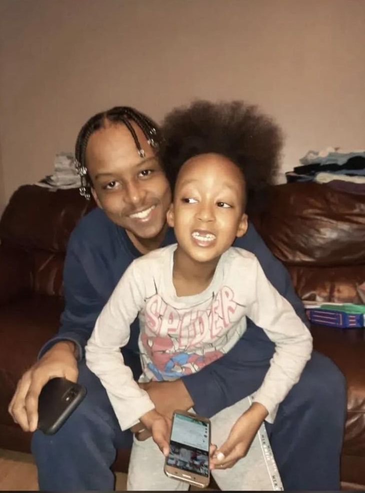 Eddie smiling on the sofa with a young child in a Spider-Man top